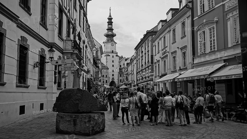 Monochrome, a group of tourists on a guided tour through the historic old town of Bratislava, street scene with a tower in the background and people in an urban area