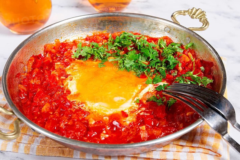 Traditional Turkish dish, scrambled eggs with tomatoes, Menemen, with herbs, in a frying pan, close-up, no people