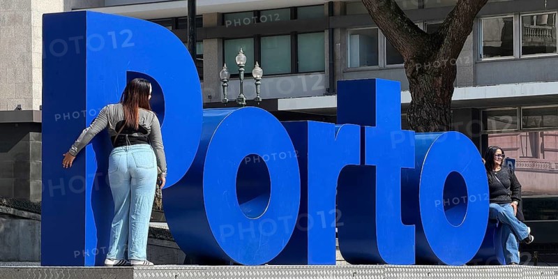 Two woman are photographed in front of the big blue Porto logo at City Hall, Câmara Municipal do Porto, Old Town, Portugal