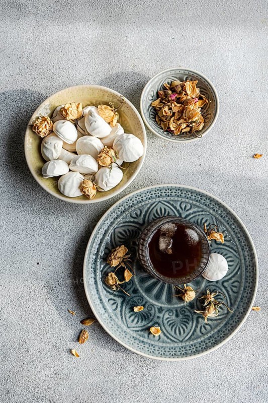 A delightful arrangement of homemade vanilla zephyr-marshmallow filled with rose jam, served alongside a chilled coffee liqueur drink with ice on a decorative plate