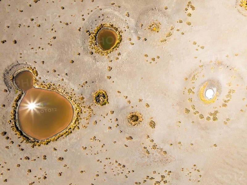 Top view, an aerial drone captures the sun reflecting in the pools of Salar de Antofalla in Catamarca, Argentina. The water bodies surrounded by salt deposits create a stunning natural pattern