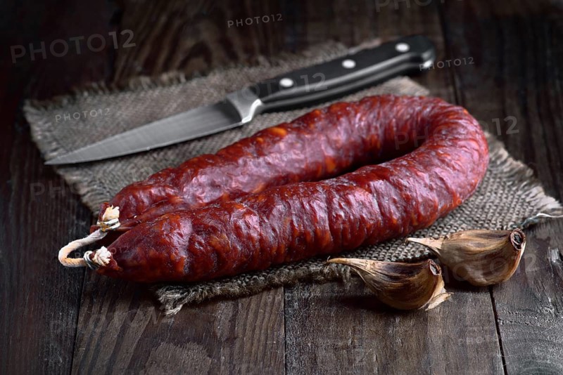 A close-up of a spanish chorizo sausage and garlic cloves on a wooden table A sharp knife adds a hint of culinary preparation Perfect for food and kitchen themes