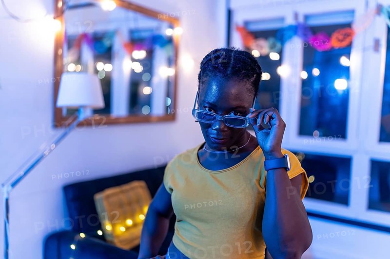 African young woman playing with sunglasses during night party at home