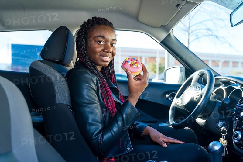 Side view of a happy african woman eating a doughnut sitting on the car