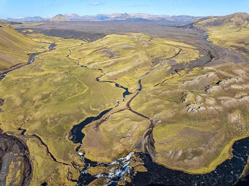 Road F232 Öldufellsleid, ford at waterfall of river bláfjallakvísl, along northern slopes of moss-covered Mt. Öldufell, Mt. Maelifell in the back, black lava sand, aerial view, Iceland