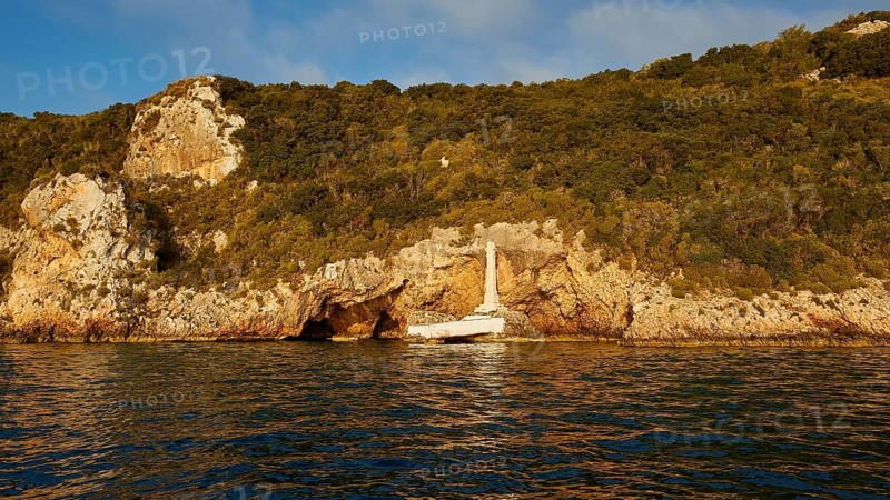 Monument to Count Santorre di Santarosa who died on May 8, 1825 in Navarino Bay defending the island of Sfaktiria. A rocky coastal landscape glows in sunlight. The sea reflects golden tones under the clear sky, morning light, Tsichli Babas islet, Sfaktiria island, Navarino Bay, Pylos, Peloponnese, Greece