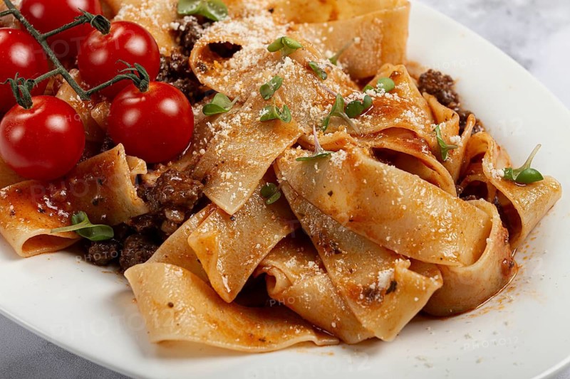 Pappardelle pasta with bolognese sauce, topped with parmesan cheese and cherry branch, homemade, no people