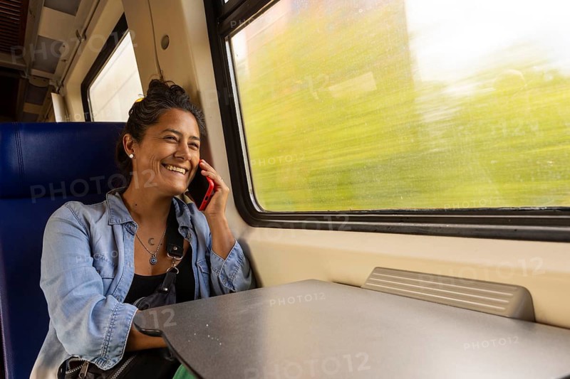 A smiling woman talks on her phone while enjoying a scenic train journey The blur of the green landscape through the window highlights the motion and excitement of travel