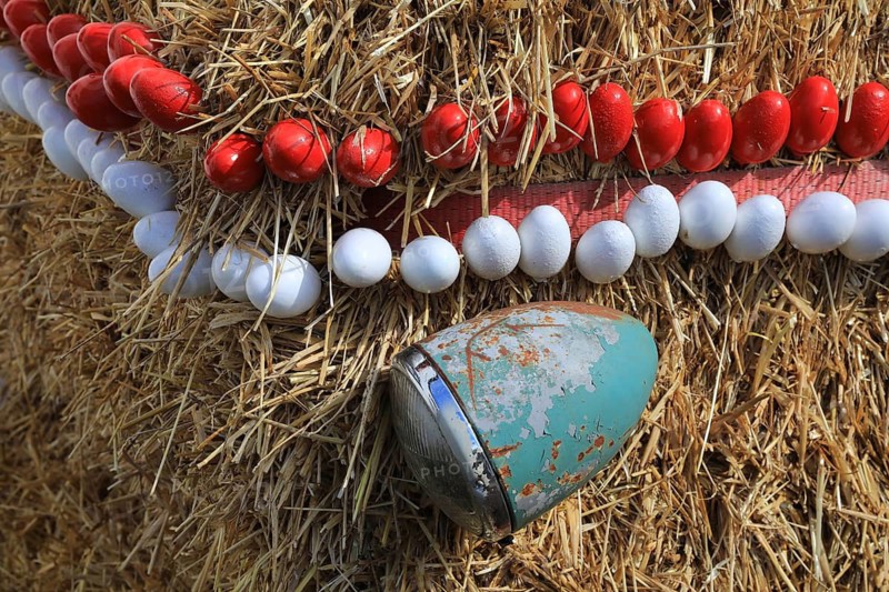Easter decoration, Franconian Switzerland, Easter fountain, here in the district of Bamberg, Upper Franconia, Bavaria, Germany, vintage tractor has been converted into an Easter fountain, detail, spotlights and garlands with eggs in red and white, close-up of a straw-clad structure with red and white tooth pattern, rusty blue fragment