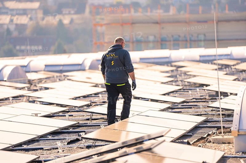 A man is inspecting solar panels on a roof, it is sunny, PV installation at OBI Baumarkt, Mühlacker, Enzkreis, Germany