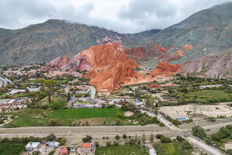 Aerial view of Purmamarca, Jujuy, Argentina, showcasing its vibrant, multicolored hills and charming village nestled in the valley, under a cloudy sky, blending nature and culture