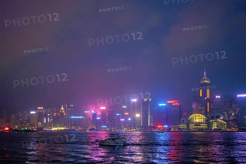 HONG KONG, CHINA, APRIL 28, 2018: Hong Kong skyline cityscape downtown skyscrapers over Victoria Harbour in the evening illuminated with tourist boat ferries, Hong Kong, China