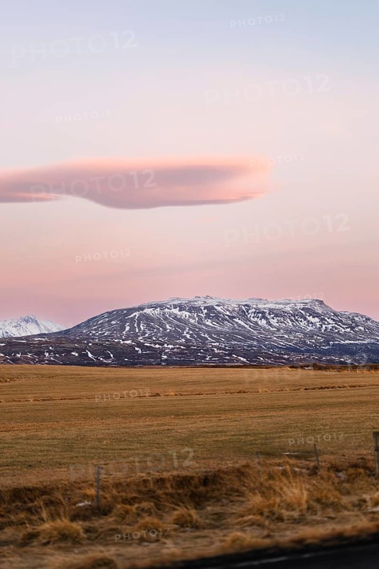 Snow-capped mountains rise majestically under a pastel sky during a serene Icelandic winter sunset. The untouched landscape reflects nature's raw beauty and tranquil ambiance