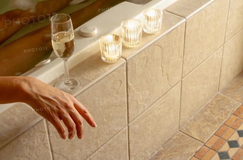 Woman relaxing in the bathroom spa tub with a glass of sparkling champagne and candles