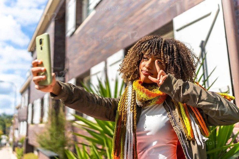 Latin woman gesturing success while taking selfie outdoors standing outside a residential street
