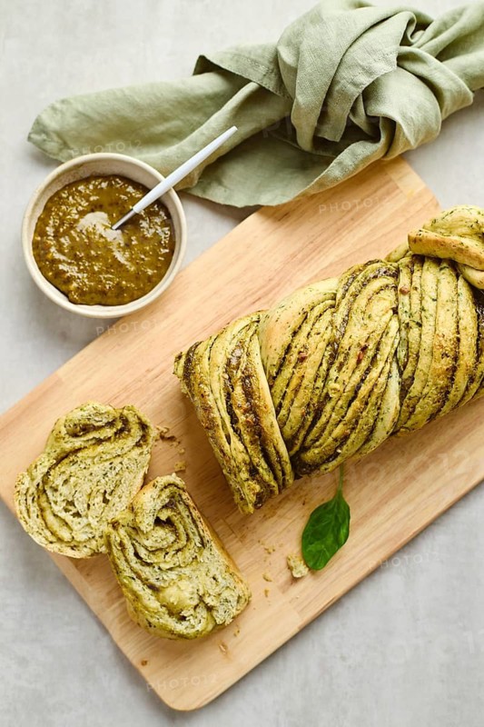 Baked homemade savoury babka plaited bread loaf flavoured with pesto on wooden bread board