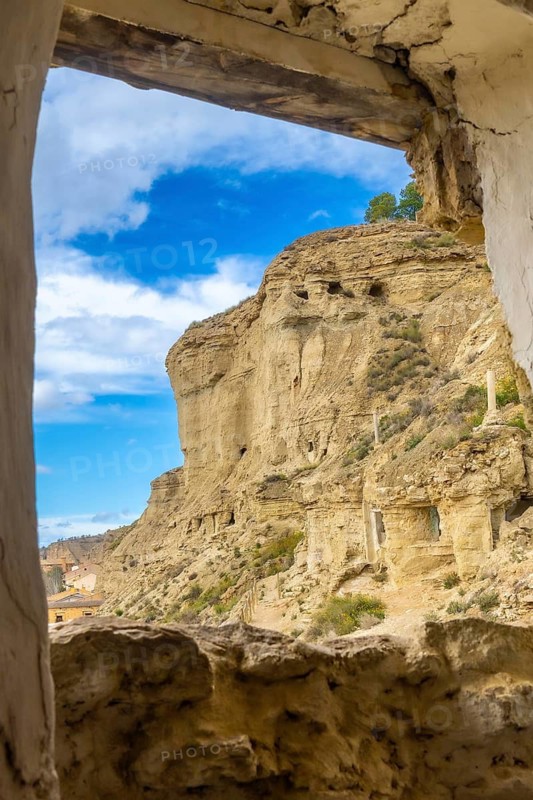 Sandstone cliffs with cave dwellings overlooking the village of arguedas in navarre, spain, seen from an old window