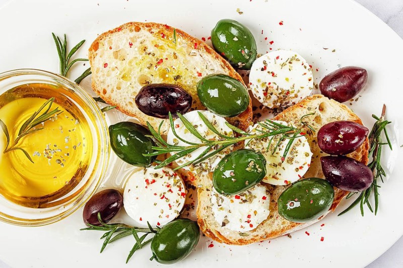 A plate with a snack, ciabatta bread with cheese and olives, olive oil, spices and herbs, top view, no people