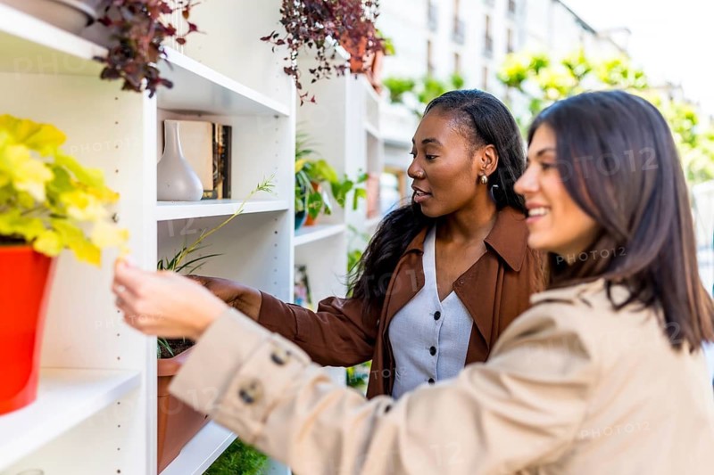 Two women selecting a variety of plants from shelves in a vibrant gardening shop, enjoying their time together while shopping for greenery