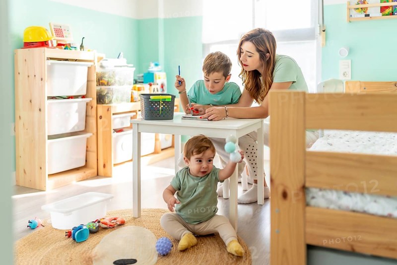 Happy single mother and sons coloring sitting in the bedroom at home