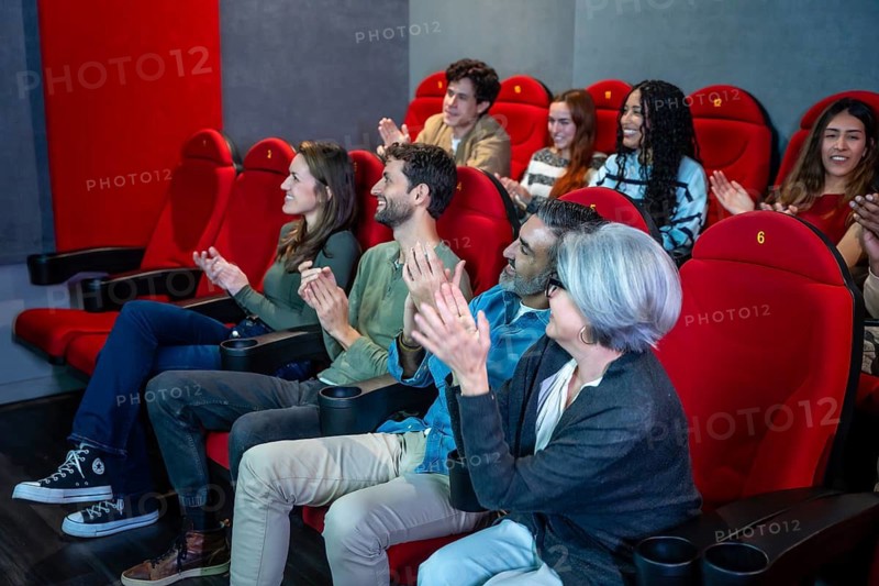 Happy moviegoers of all ages and ethnicities are applauding enthusiastically at the end of a film, enjoying a shared cultural experience