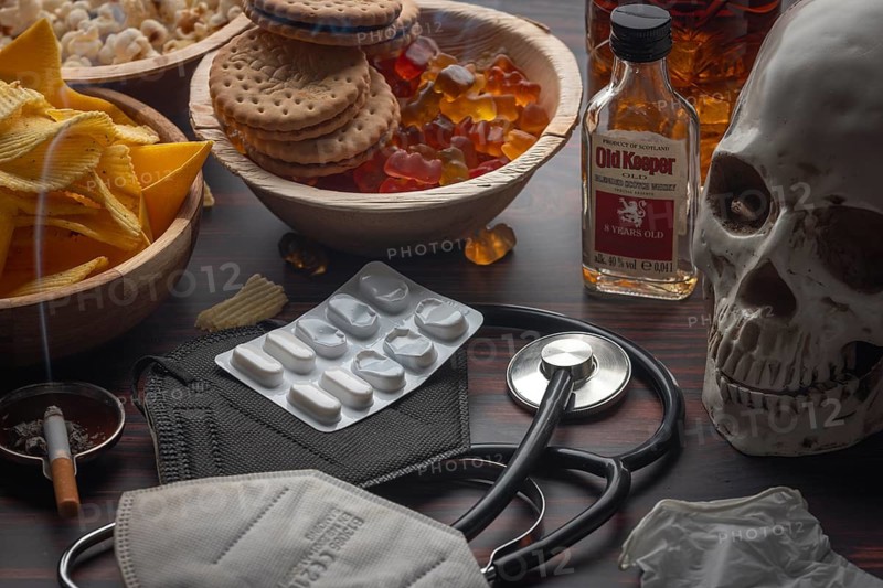 Skull with cigarette and pills next to jelly babies, crisps and alcohol