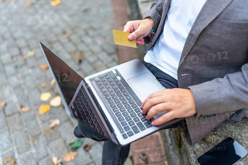 Close-up top view of an unrecognizable businessman using credit card to shop online outdoors sitting on a bench