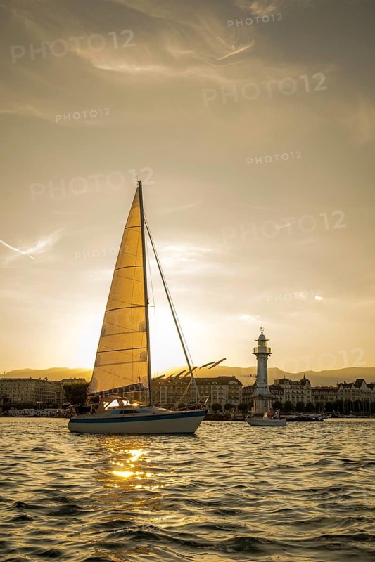 A serene sunset scene at Lake Geneva, with a sailboat gracefully gliding near a historic lighthouse, both bathed in golden light