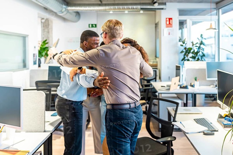 Group of diverse colleagues embracing each other, celebrating a successful project in a modern coworking office