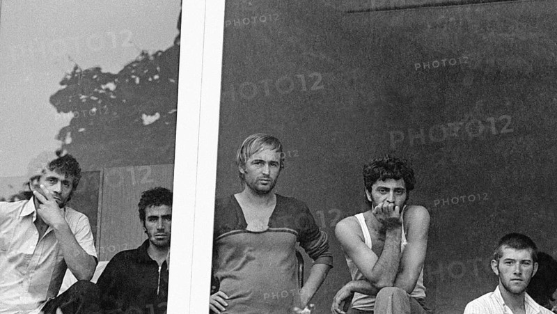 Geseke, DEU - 15.07.1990 - Albanian refugees look out a window at the regional office for refugees in Unna-Massen. The Albanians had fled to the German embassy in Tirana and were then approved as a contingent to travel to Germany, Geseke, Germany