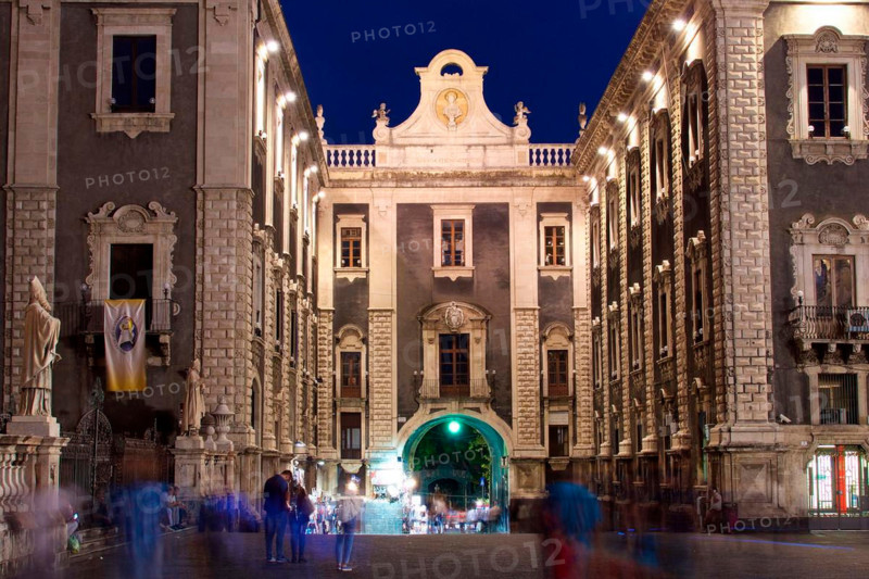 Long exposure, blurred passers-by, illuminated historical buildings, gateway, night shot, baroque old town, Catania, east coast, Sicily, Italy