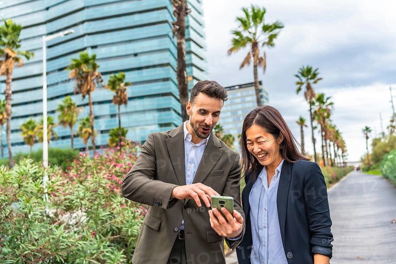 Caucasian businessman and happy asian businesswoman using phone walking along a financial area in the city
