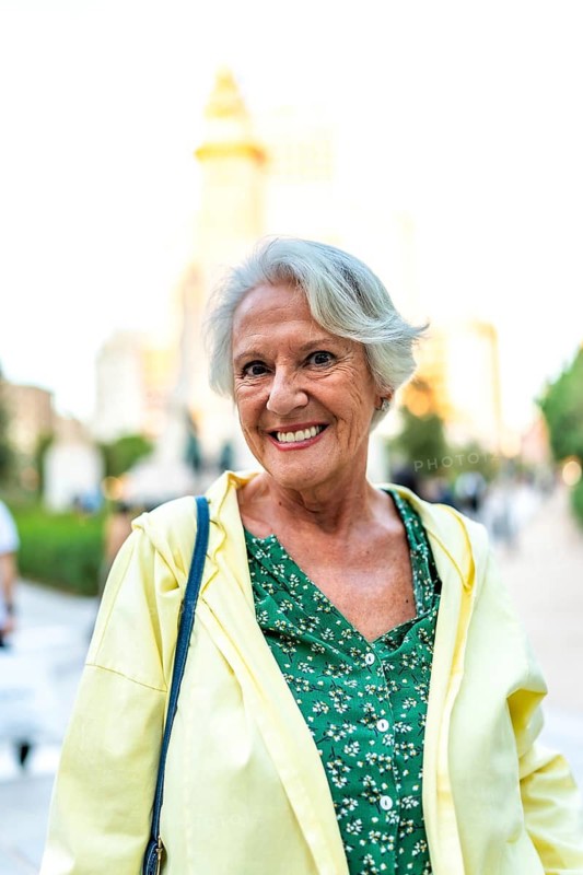 Vertical close-up portrait of a happy elder modern woman standing in the city smiling at camera