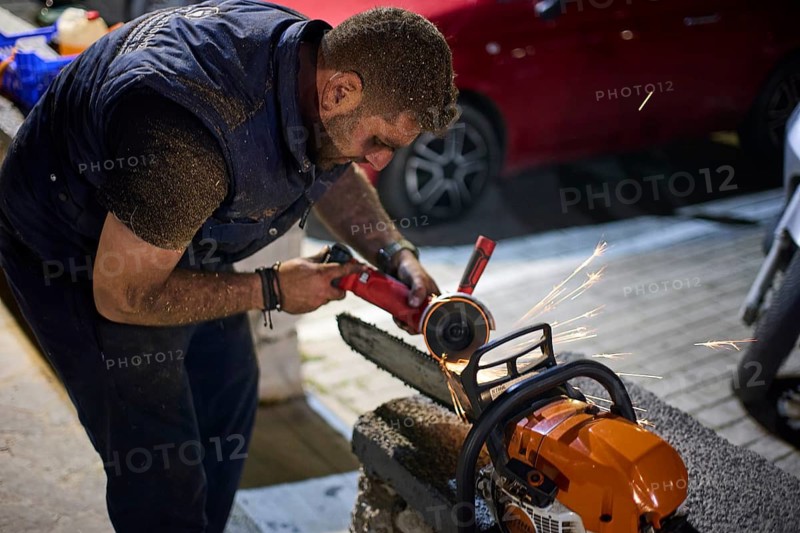 ©Udo Rein, A man uses a grinding machine at night to sharpen the teeth of a chainsaw, Easter fire Psinthos, Holy Saturday, Easter, Psinthos, Rhodes, Dodecanese, Greek Islands, Greece