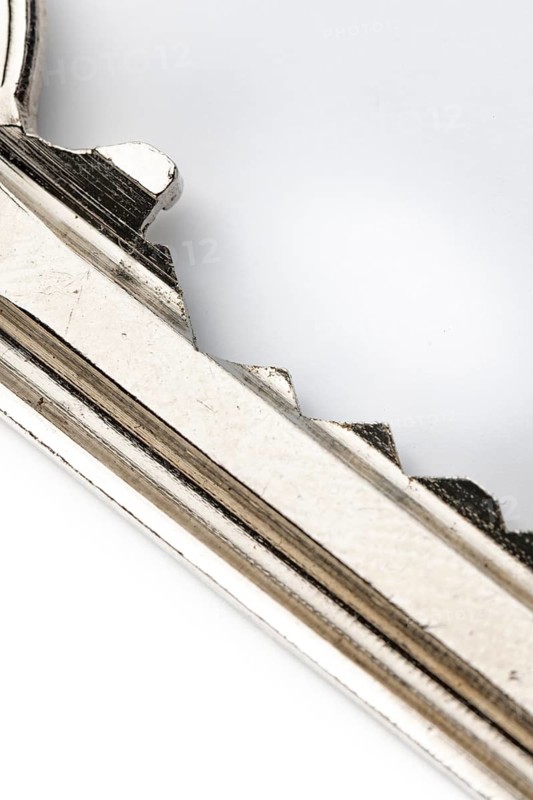 Macro image of the teeth of a used silver metal key, white background