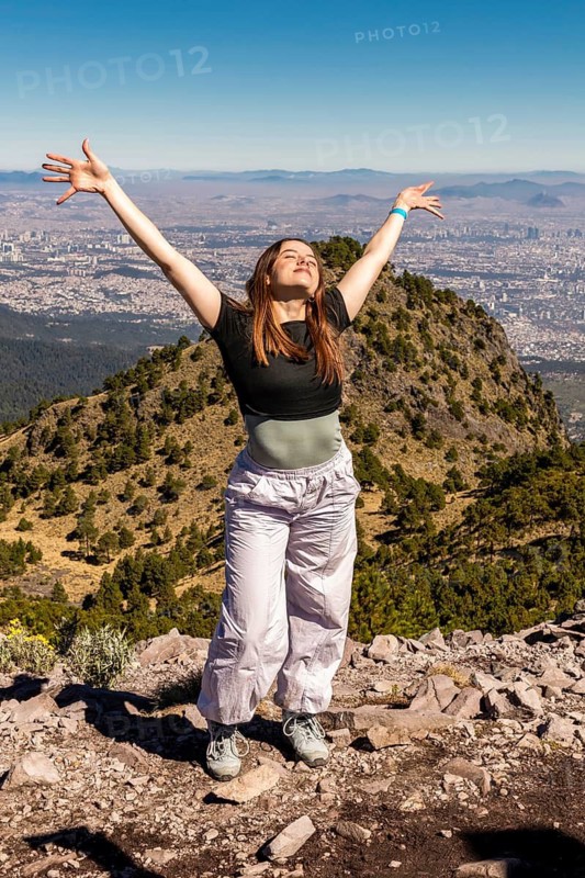 A joyful person with arms outstretched stands on a rocky mountain peak, enjoying panoramic views and the beauty of nature, symbolizing freedom and adventure