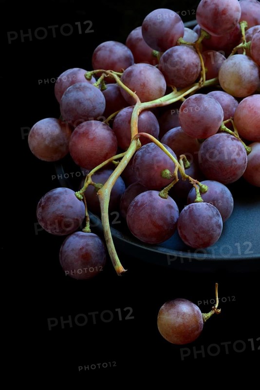 Red grape vine (Vitis vinifera) on plate against dark background