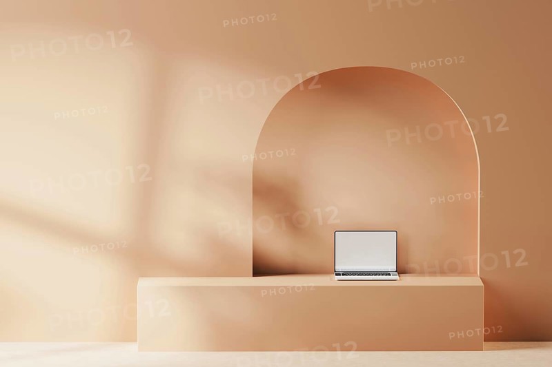 A sleek laptop is placed on a smooth surface against a soft, geometric backdrop. The warm tones create a serene atmosphere ideal for focused work or creativity