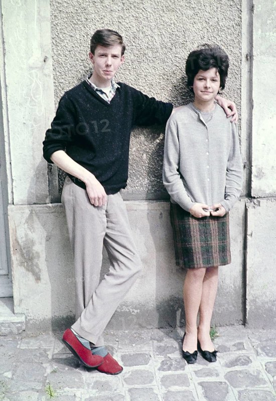 Young man casual smart clothing red slippers with his arm around shoulder of slim pretty young woman against wall of building, France c 1960