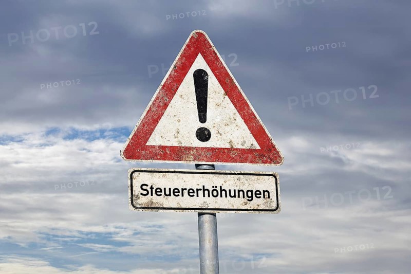(photo montage) Sign with text TAX INCREASES under a road sign Danger location exempted in front of a sky