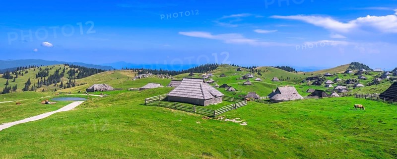 Traditional wooden shepherd's huts scattered across the picturesque velika planina plateau, framed by the kamnik savinja alps under a summer sky