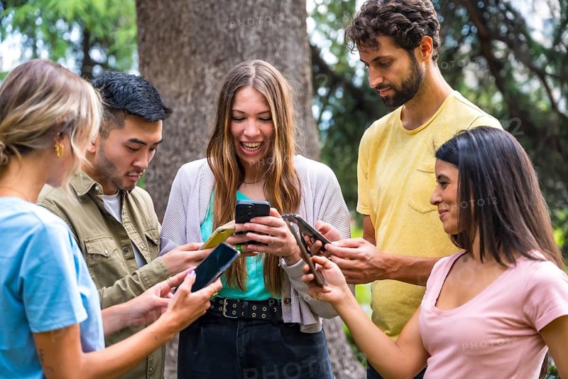 Multiethnic group with phones watching internet or social networks in the park, technology concept