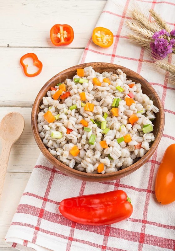 Pearl barley porridge with vegetables in wooden bowl on a white wooden background and linen textile. Side view, close up. Russian traditional cuisine