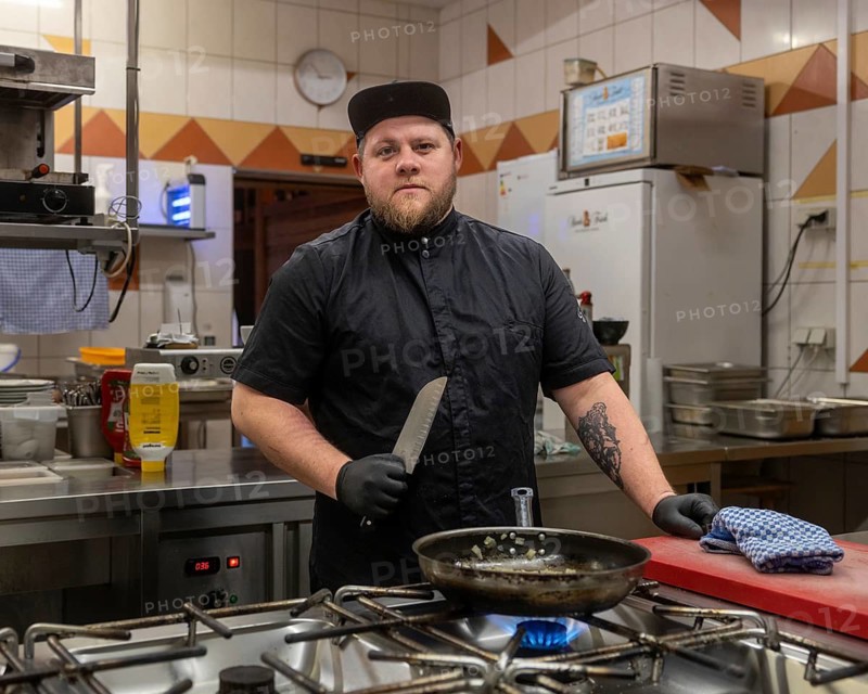 A focused chef in a professional kitchen setting, holding a knife with confidence. The kitchen is fully equipped, and the chef is ready to prepare a gourmet meal