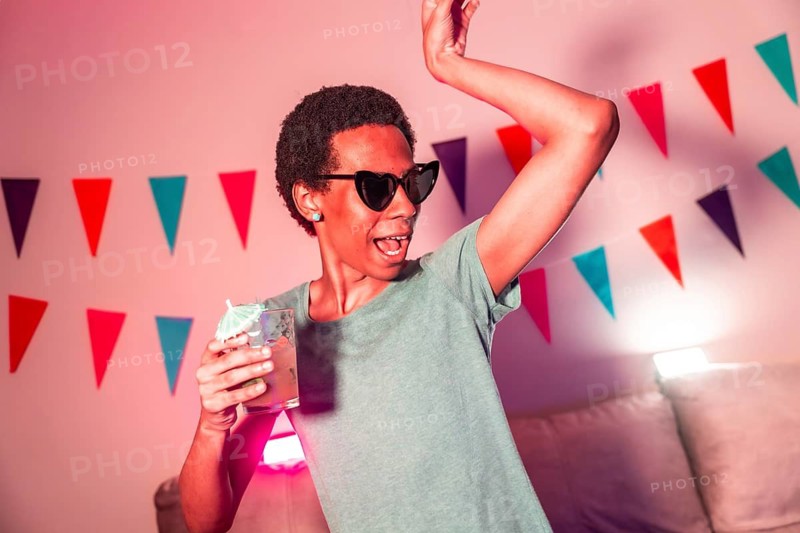 Cool latin man dancing and drinking cocktails partying at night with colorful neon light illuminating the apartment