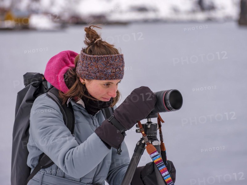 Photographer with coat and gloves on camera on tripod, Lofoten, Norway