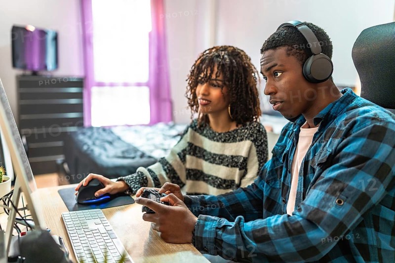 Young man and woman enjoying their time together, playing video games on a computer and gamepad while relaxing at home