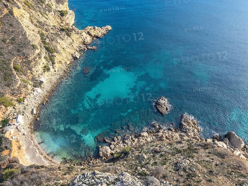 Aerial view of the stunning Costa Blanca coastline, capturing the rich blue waters of the Mediterranean Sea contrasting with the rugged cliffs and rocky shoreline at sunrise