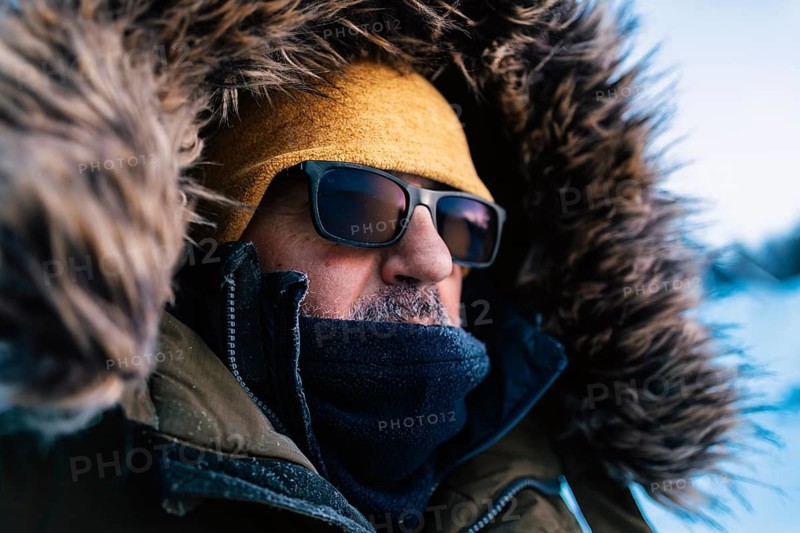 An adventurer warmly dressed in a fur-lined hood and sunglasses faces the harsh yet beautiful winter environment of Swedish Lapland, ready for adventures in the snow