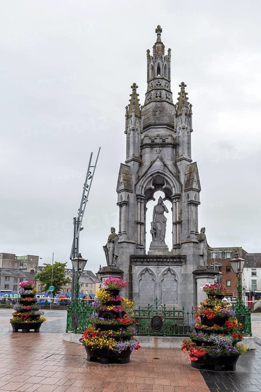 Large stone monument with colourful flowers in a town square, Cork